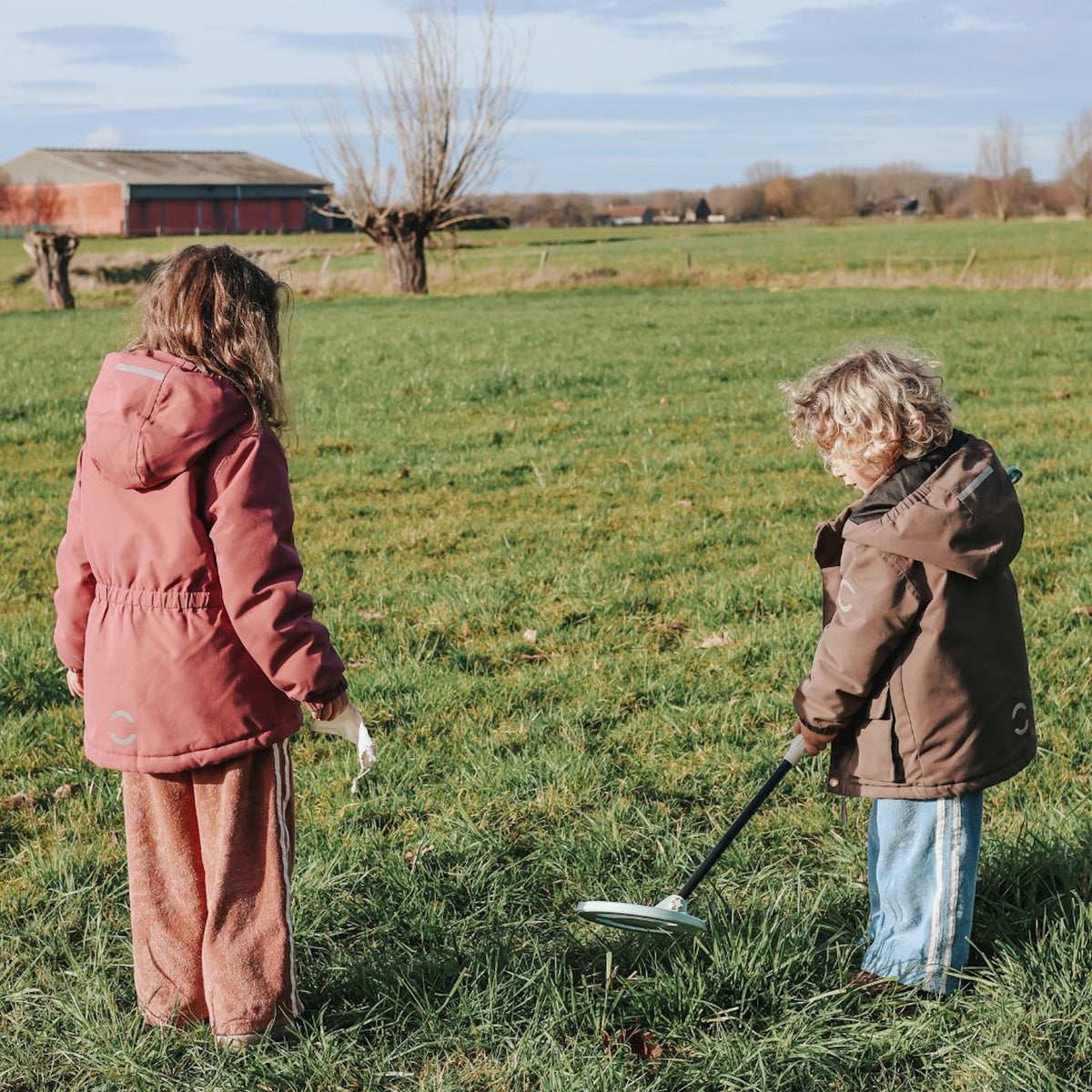 Two kids playing with a toy metal detector in a grassy green field on a clear day.