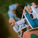 Child holding a Kidywolf K-Print camera showing an instant black and white thermal photo print outdoors.
