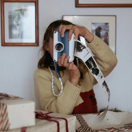 Young girl using a blue Kidywolf Kidyprint instant camera to print a long strip of black and white thermal photos.