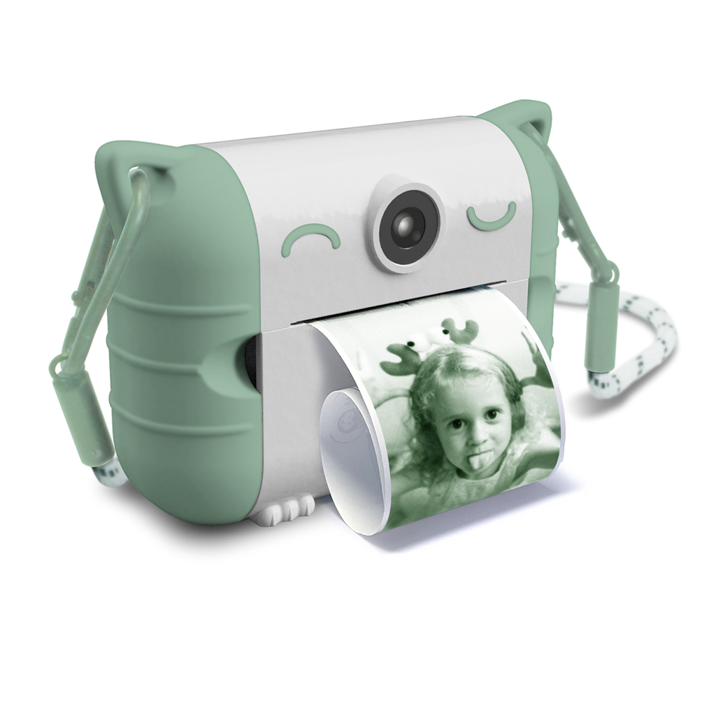 Cute white and mint green instant camera with cat ears prints a photo of a child making a playful face. The design is whimsical and fun.