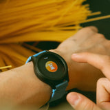 A person sets a timer on a smartwatch, with spaghetti noodles in the background.