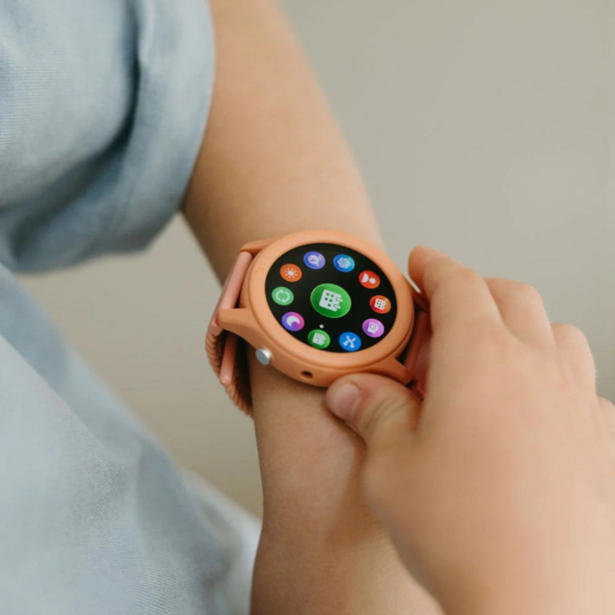 A child wearing a coral pink K-Watch interactive smartwatch, displaying various colorful app icons.
