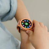 A child wearing a coral pink K-Watch interactive smartwatch, displaying various colorful app icons.