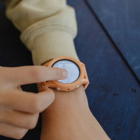 A child's hand touching the screen of a coral-colored smartwatch worn on a wrist.
