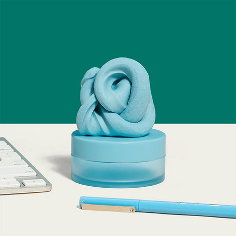 Sky-blue focus putty on its container, sitting on a desk next to a keyboard and pen.