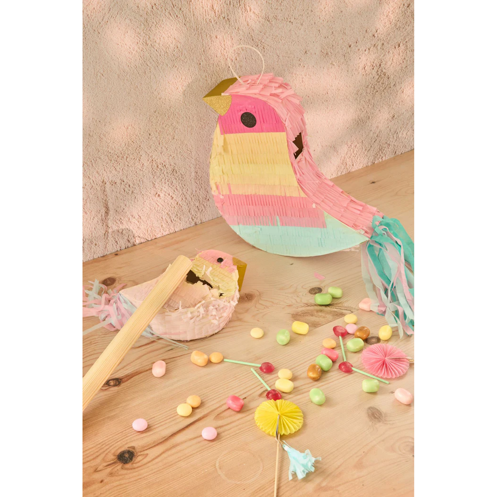 Cute bird-shaped piñata in pastel colors on wooden table with colorful candies and broken pieces. Playful and festive atmosphere.