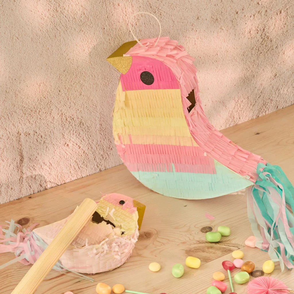 Cute bird-shaped piñata in pastel colors on wooden table with colorful candies and broken pieces. Playful and festive atmosphere.