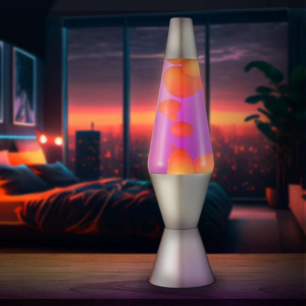 A glowing lava lamp with orange and pink wax blobs sits on a wooden table. It's set against a cozy bedroom backdrop with a large window and city lights at sunset.