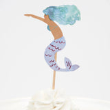 Watercolor mermaid cupcake topper with blue-green hair and a purple tail, stuck into white frosting.