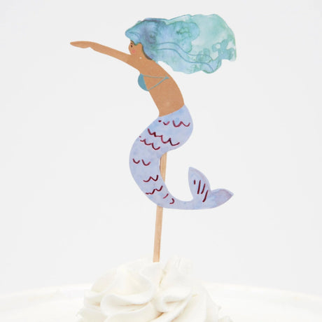 Watercolor mermaid cupcake topper with blue-green hair and a purple tail, stuck into white frosting.