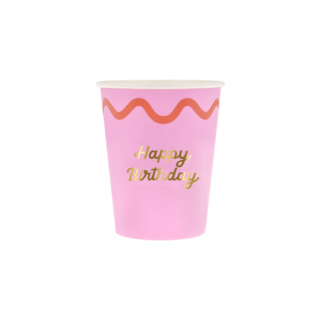 A pink paper cup with an orange wavy border and "Happy Birthday" written in gold script.