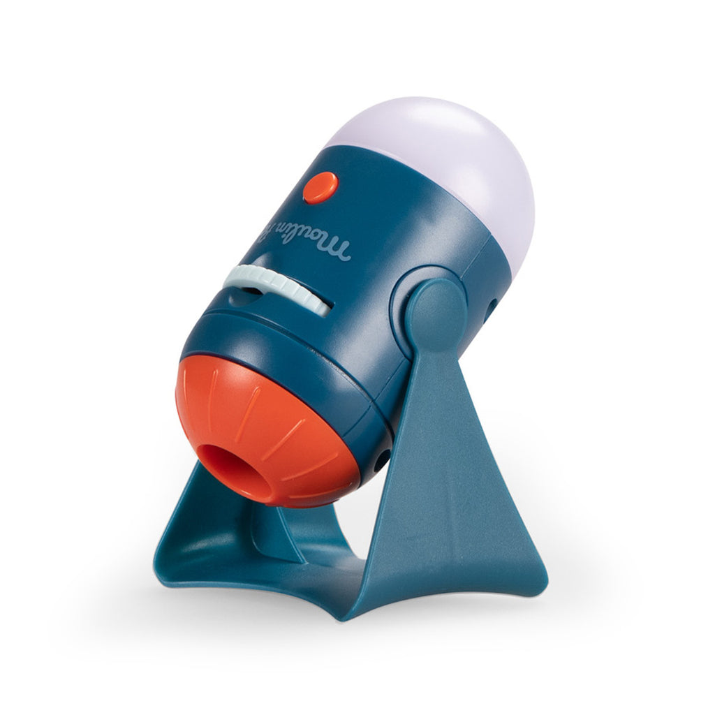 A small, colorful projector shaped like a rocket with a blue body, orange front, and a clear top, mounted on a blue stand against a white background.