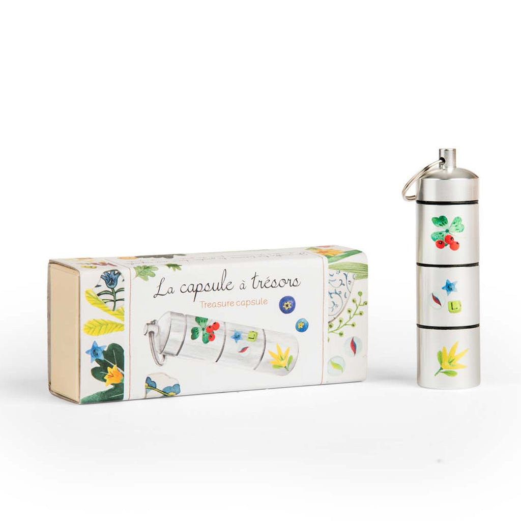 Metallic cylindrical capsule with colorful nature motifs next to a matching box labeled "La capsule à trésors" (Treasure capsule), conveying a whimsical tone.
