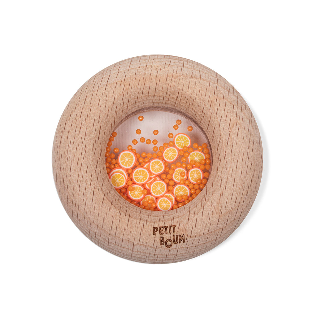A round wooden sensory toy with a clear window, filled with tiny orange fruit slice decorations.