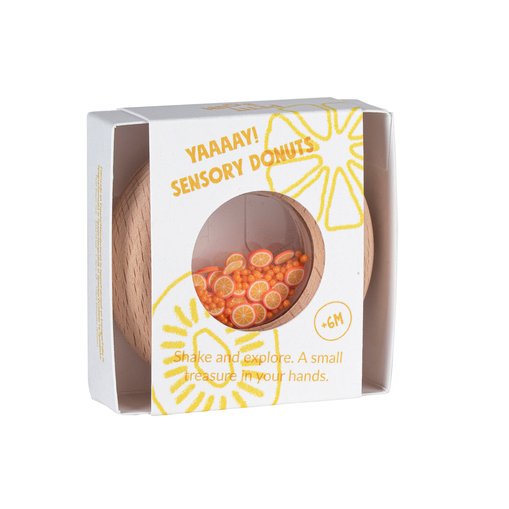 A Petit Boum orange-themed wooden sensory donut in its packaging, featuring bright orange fruit slices inside a clear window.