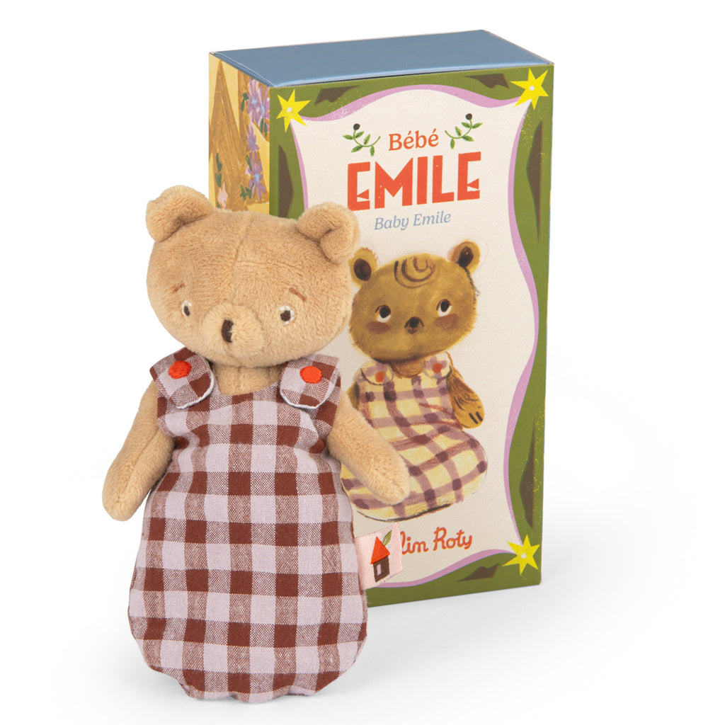 A plush bear in a checkered dress stands in front of a colorful box labeled "Bébé Émile." The scene exudes a playful and nostalgic charm.