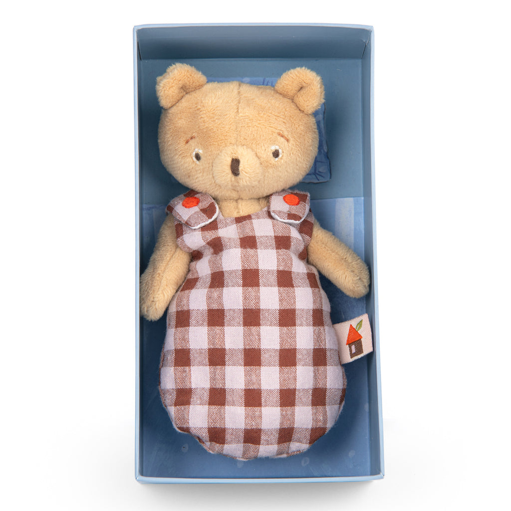 A plush teddy bear wearing a brown and white checkered dress with orange button details. The bear, with a gentle expression, has a small fabric tag on the side.