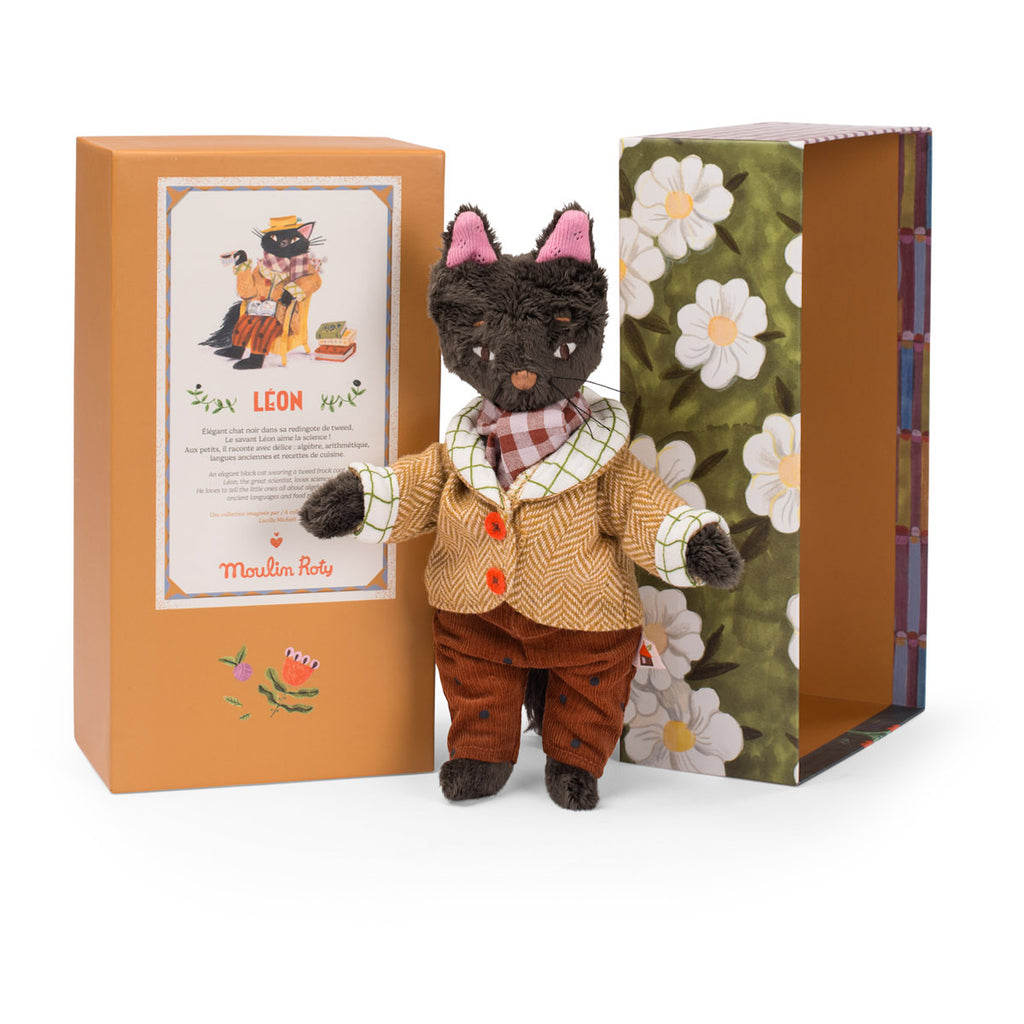 Stuffed cat toy in vintage clothing stands beside an open floral-patterned box. The cat wears a plaid scarf, brown pants, and a tan jacket.