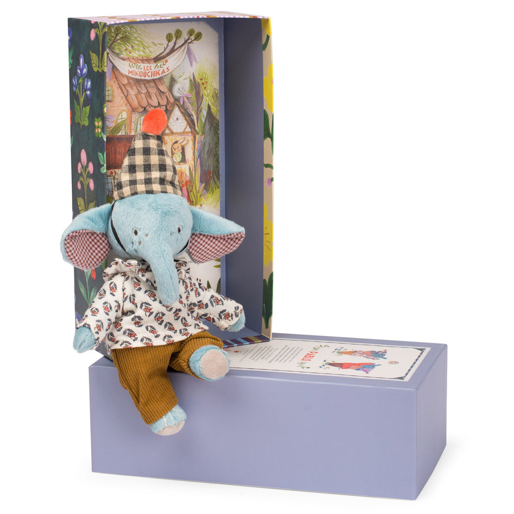 A blue stuffed elephant with a patterned shirt and plaid hat sits on a purple box. The colorful box features whimsical, floral illustrations.