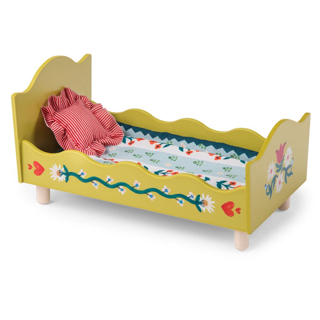 A small, decorative wooden doll bed painted yellow with floral designs. It features a red-striped pillow and a colorful floral-patterned mattress.
