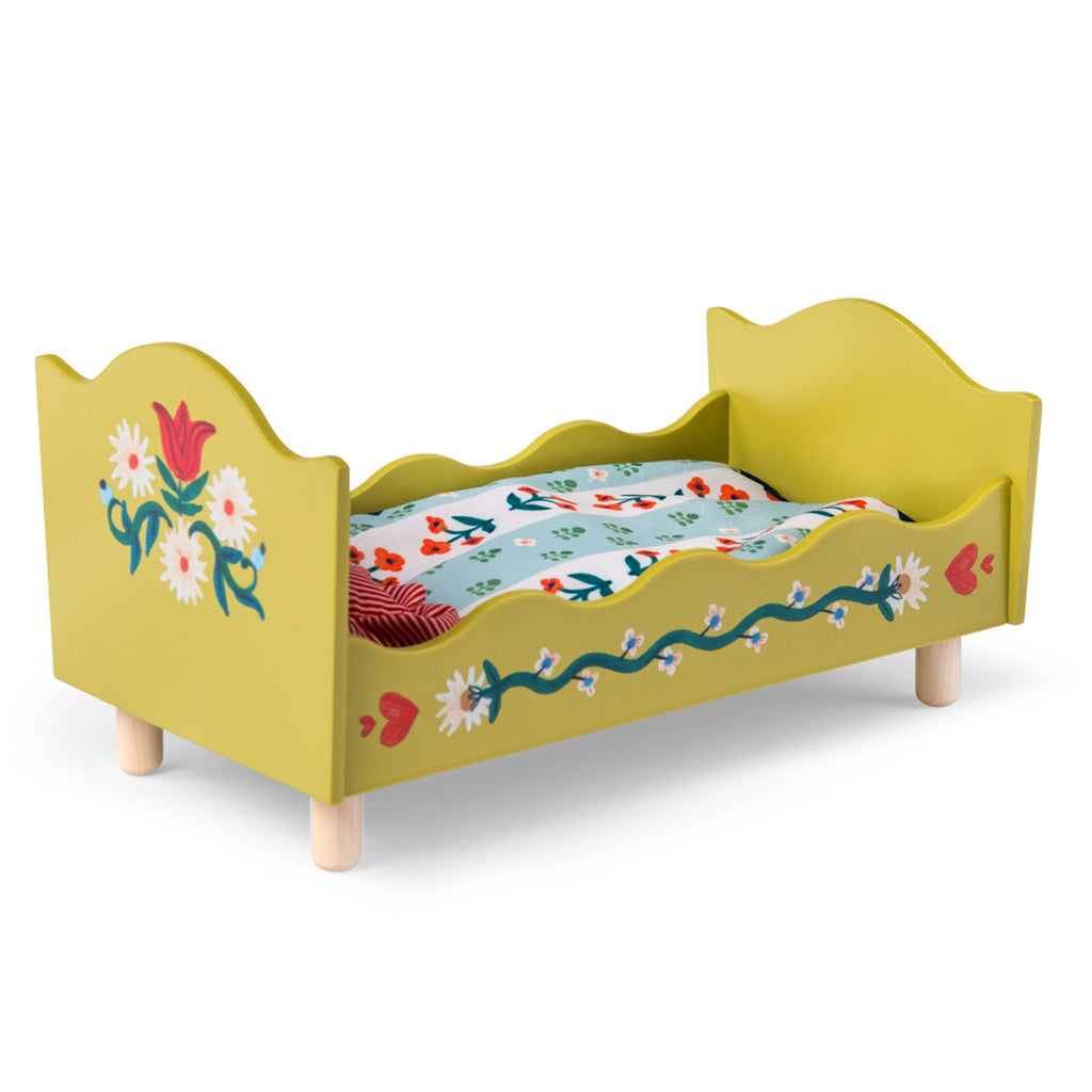 A small, decorative wooden doll bed painted yellow with floral designs. It features a red-striped pillow and a colorful floral-patterned mattress.
