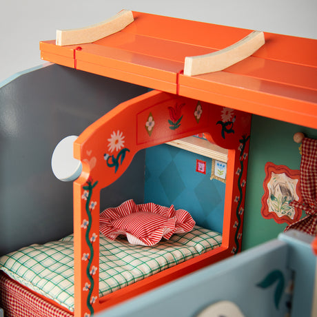 Wooden toy caravan interior featuring a miniature bed with green plaid bedding and a red striped pillow.