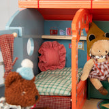 Toy caravan dollhouse interior with miniature bed, striped pillow, and plush animal figures.