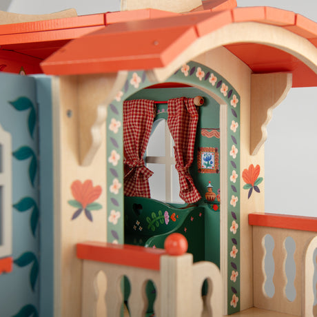 Decorative wooden toy caravan house featuring colorful folk art, floral designs, and red gingham curtains.