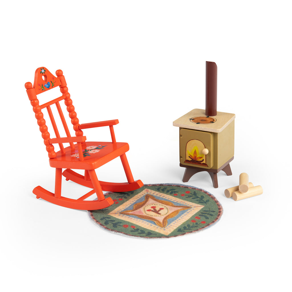 A small, bright orange rocking chair with floral designs, a brown wood stove with an open door, a pile of logs, and a colorful round rug. Cozy atmosphere.