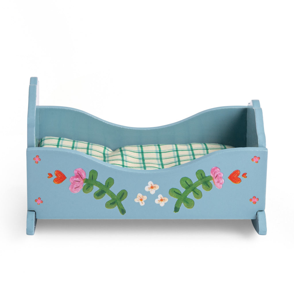 Blue wooden toy bed with floral and deer designs, featuring a grid-patterned mattress. The bed has a playful, whimsical charm.