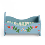 Blue wooden toy doll cradle with floral painted details and a green plaid mattress on a white background.