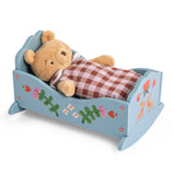 Plush teddy bear sleeping under a plaid blanket in a blue wooden toy cradle.