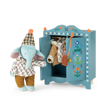 Plush elephant doll next to a blue wooden toy wardrobe filled with doll clothes.