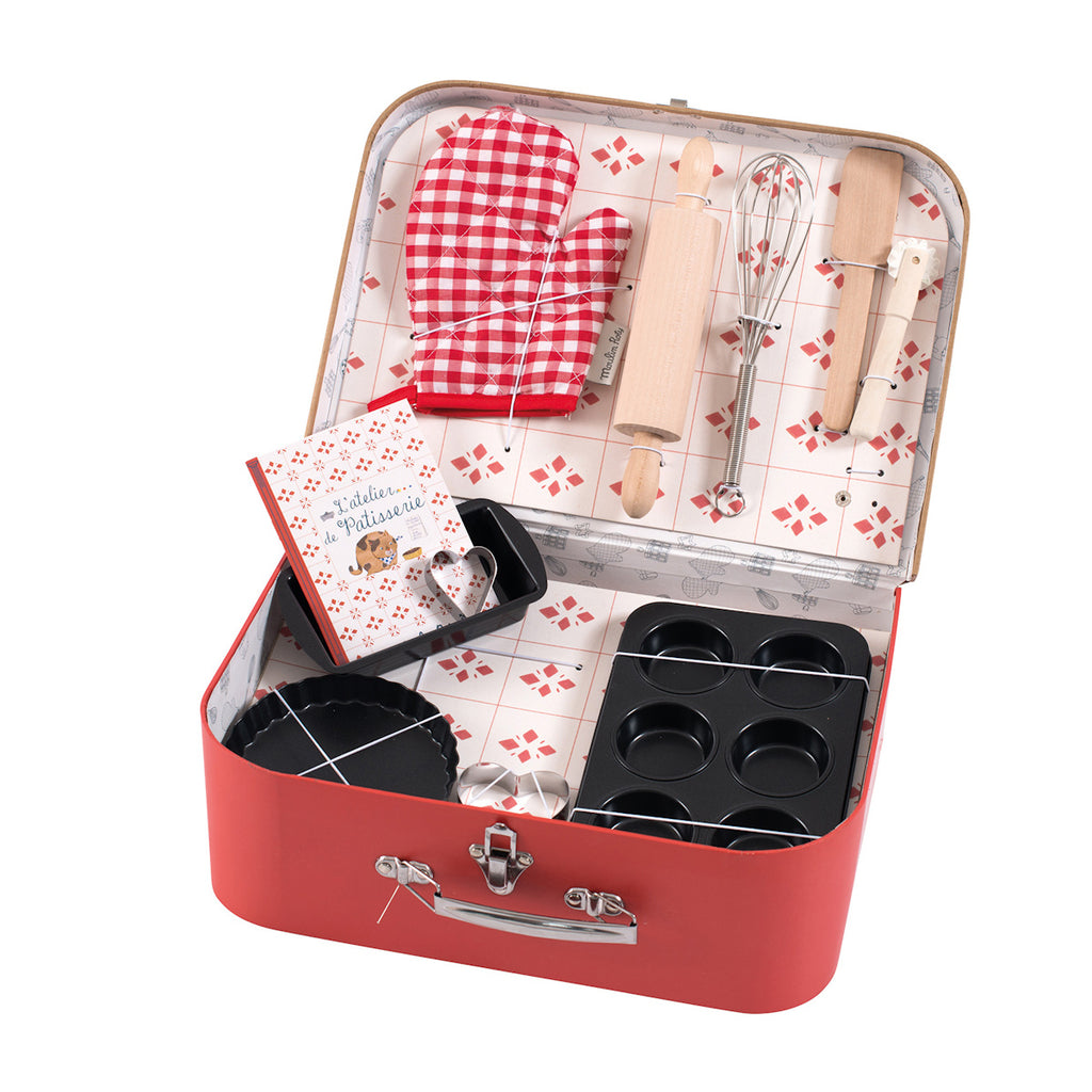 A red suitcase with baking tools, including a rolling pin, whisk, spatula, muffin tray, tart pan, cookie cutters, mitt, and a recipe book.
