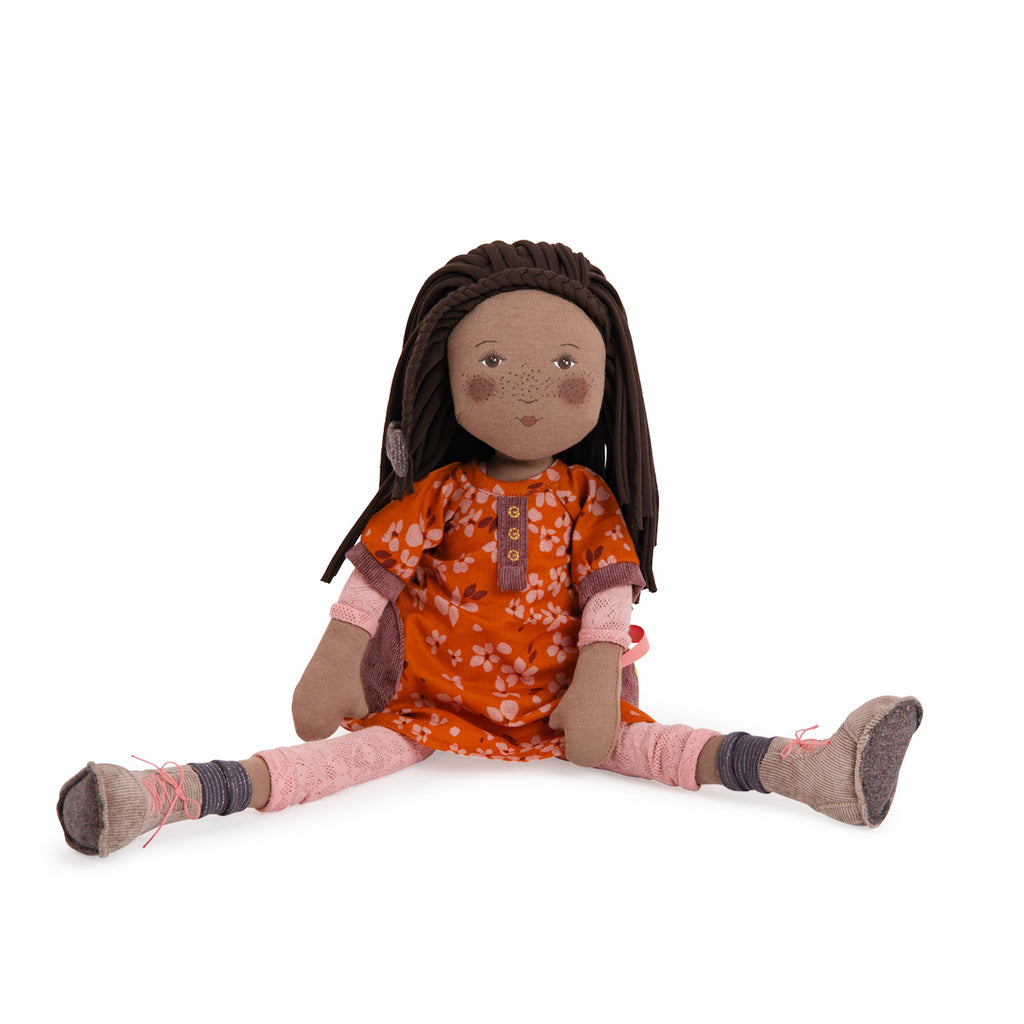 Fabric doll with brown hair and embroidered face, wearing an orange floral dress and pink leggings. The doll sits with legs spread and a gentle smile.