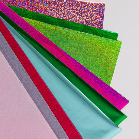 Colorful holographic craft paper and fantasy boards layered in pink, green, and blue.