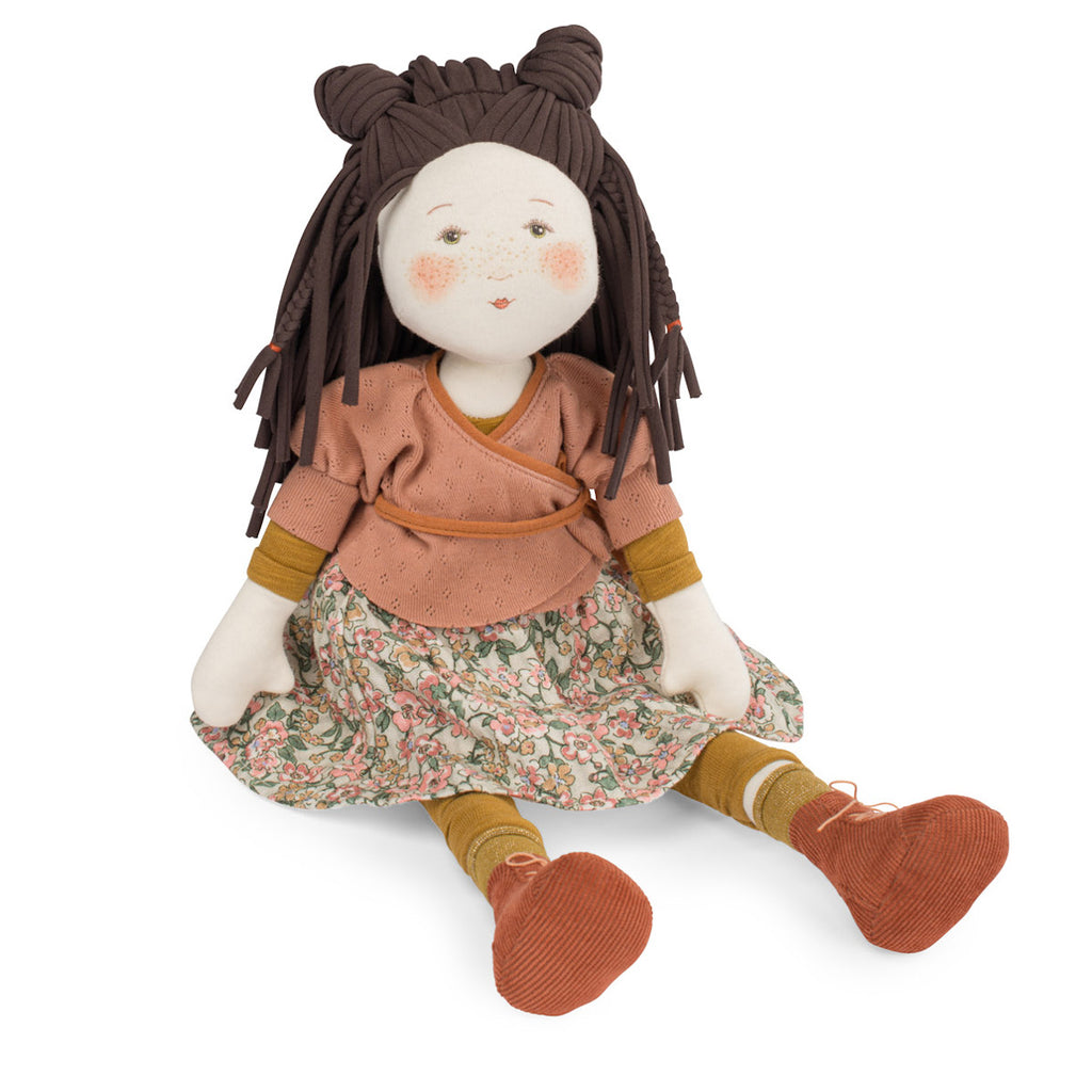 A plush doll with brown braided hair in two buns, wearing a peach top, floral skirt, yellow socks, and orange shoes. The doll's face is cheerful.