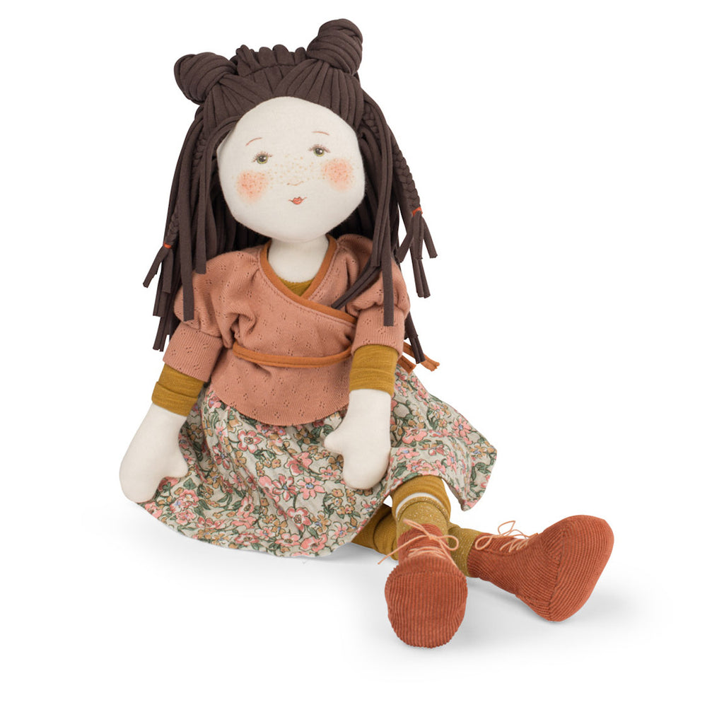 A plush doll with brown braided hair in two buns, wearing a peach top, floral skirt, yellow socks, and orange shoes. The doll's face is cheerful.