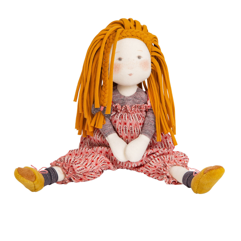 A cloth doll with orange yarn hair, wearing a red patterned dress, gray top, and yellow shoes. The doll sits with legs outstretched, exuding a cute and playful vibe.