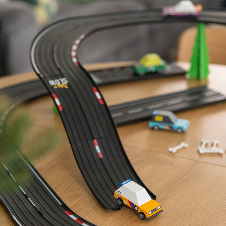 Candylab Candycar wooden toy cars racing on a black slot car track, including the Rascal, a police car, and a green taxi.