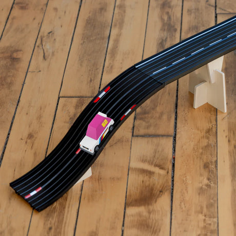 Candylab Roadworks Hop expansion pack with a toy car on an elevated black track over a wooden floor.