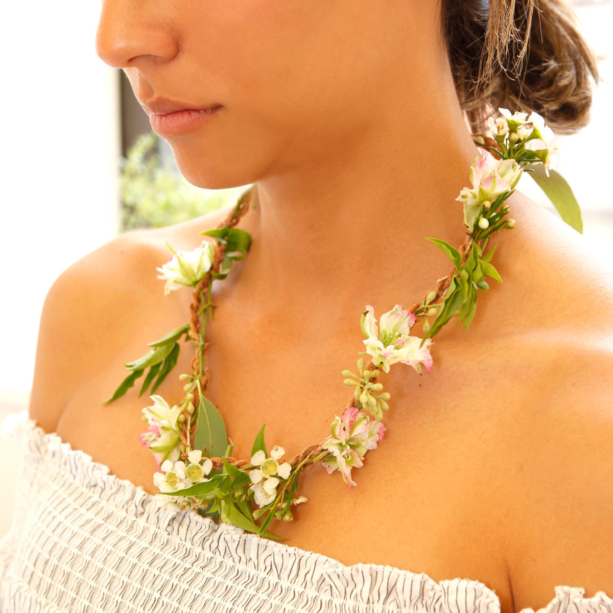 A woman wearing a Huckleberry DIY fresh flower necklace with white and pink blossoms on a braided tan cord.