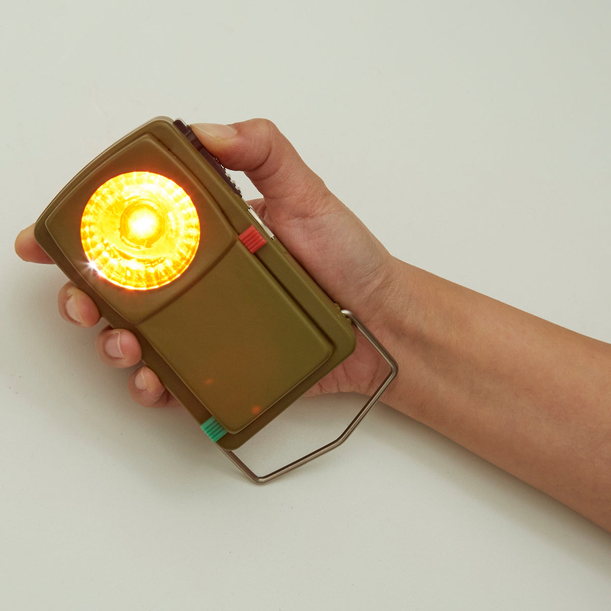 Huckleberry Morse code signal light in use, featuring a hand holding it and the amber light shining.