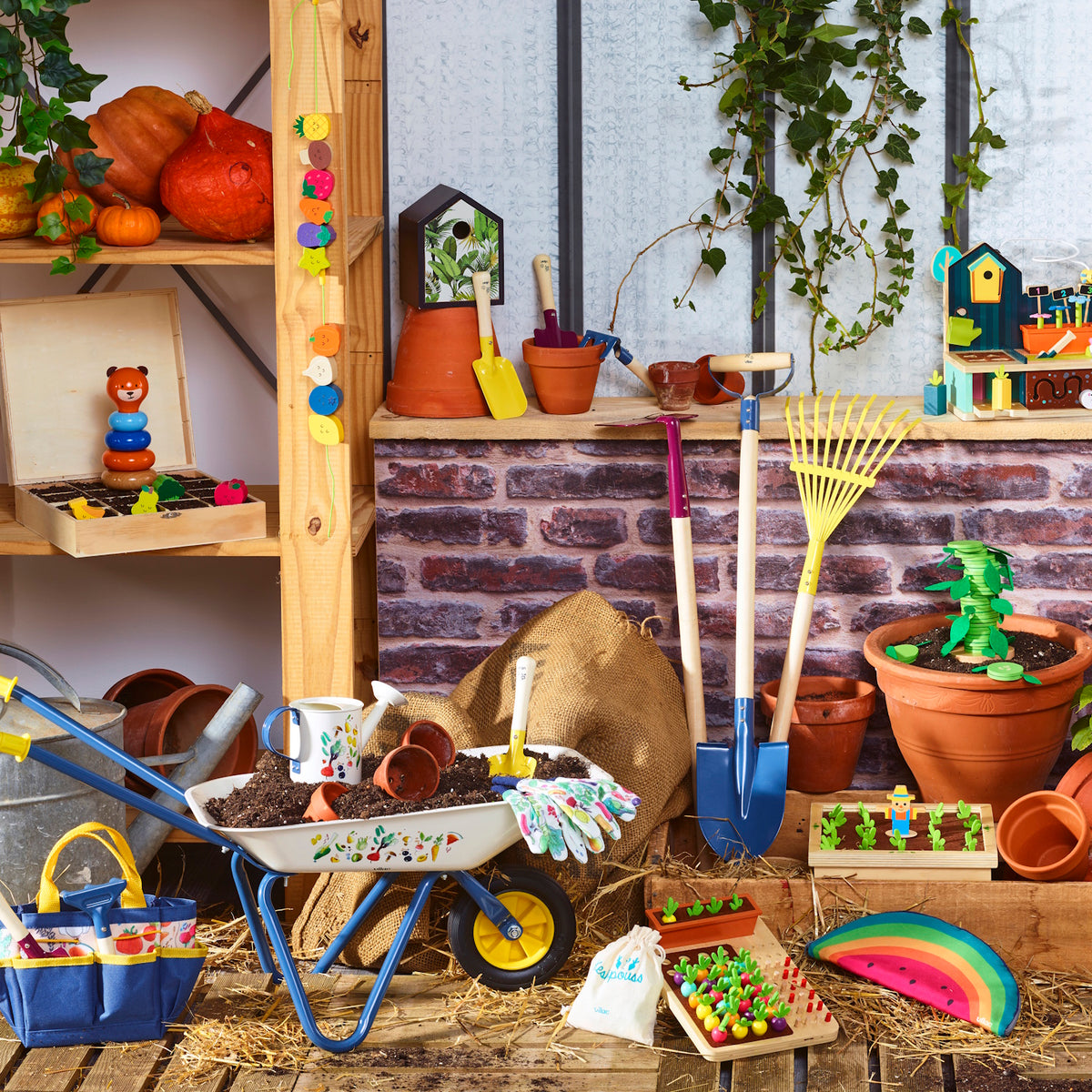 Kids gardening set with wheelbarrow, shovel, rake, and watering can displayed with potting soil and colorful wooden toys.