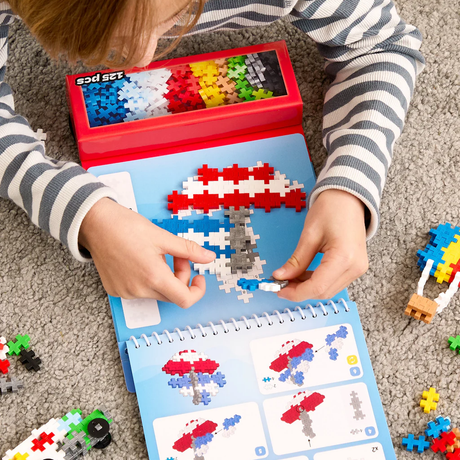 Child building a colorful Plus-Plus sailboat on a blue activity pad using the 125-piece transportation set.