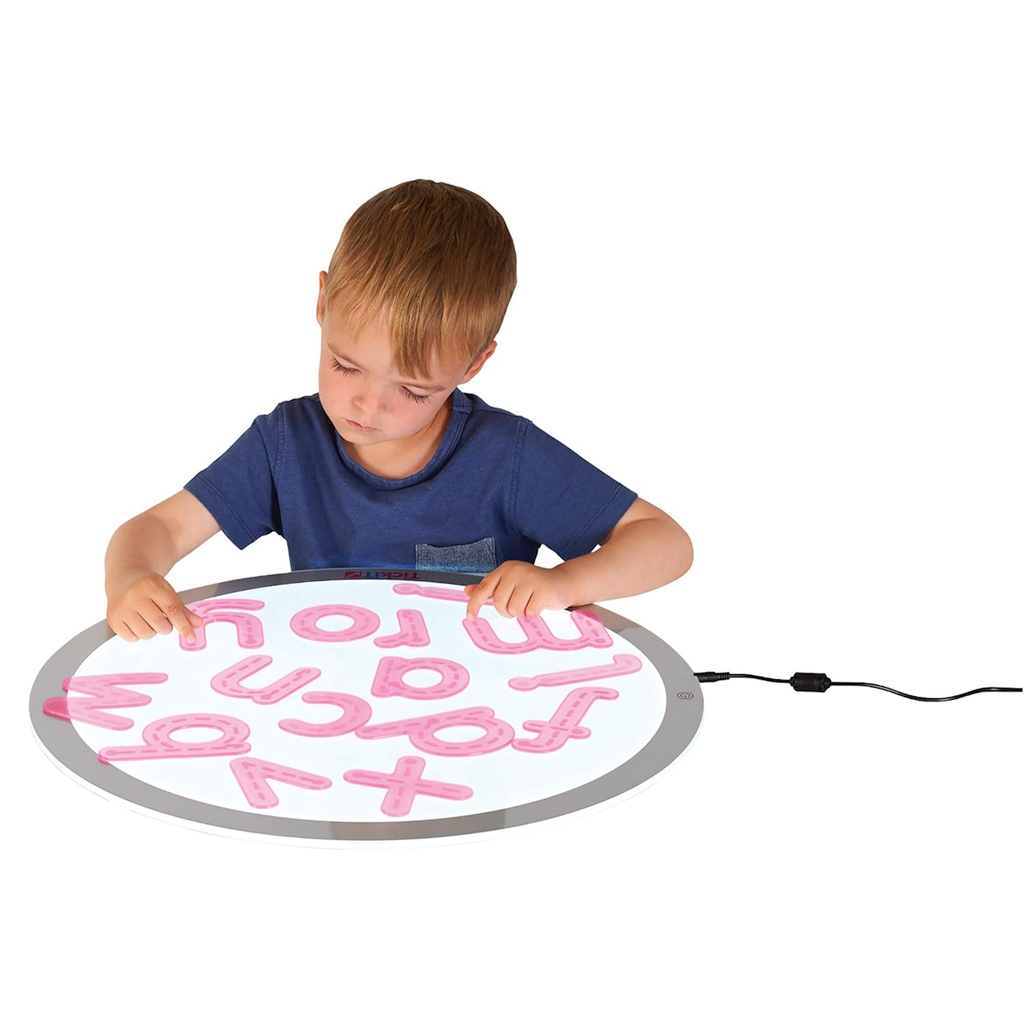 A child in a blue shirt is focused on arranging pink letters on a round, illuminated lightboard. The tone is educational and engaging.