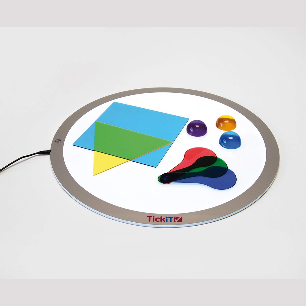 Round light panel with colorful translucent shapes: blue square, green triangle, yellow triangle, and colored discs. Bright, educational setting.