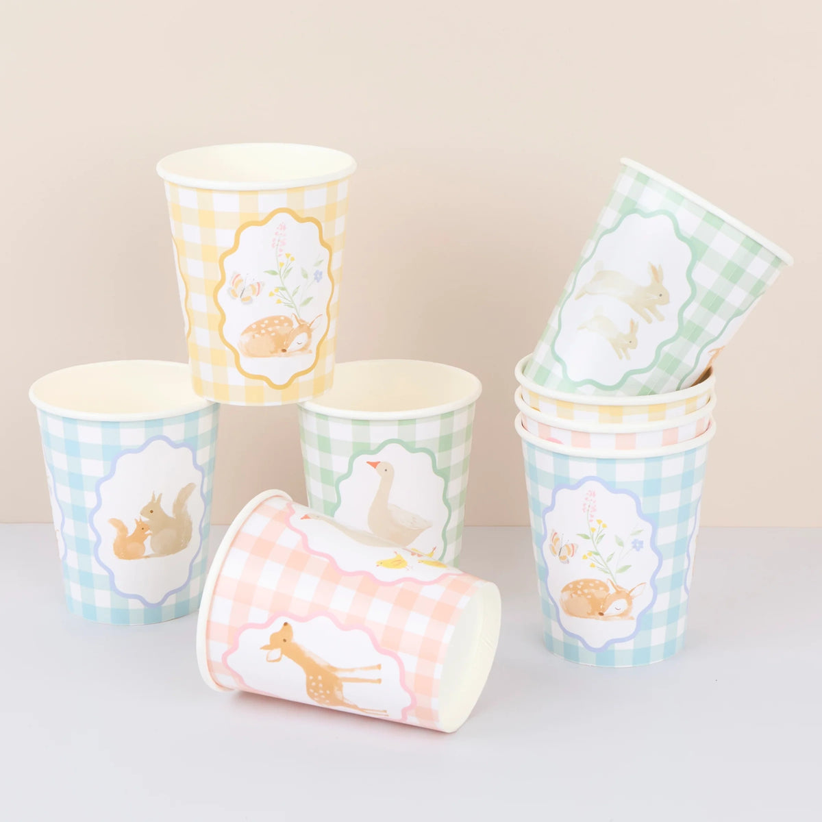 A stack and cluster of pastel gingham paper cups featuring cute woodland animal illustrations.