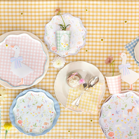 Flat lay of pastel goose and woodland-themed party plates, cups, and a cupcake on a yellow gingham tablecloth.