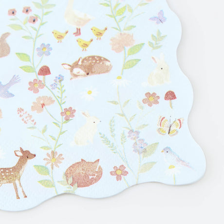 Light blue scalloped napkin with pastel illustrations of woodland animals, birds, flowers, and mushrooms.